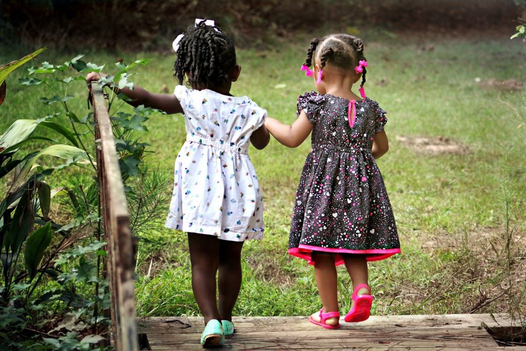 Mała dziewczynki trzymajace sie za ręce idą w dziecięcych butach przez drewniany most